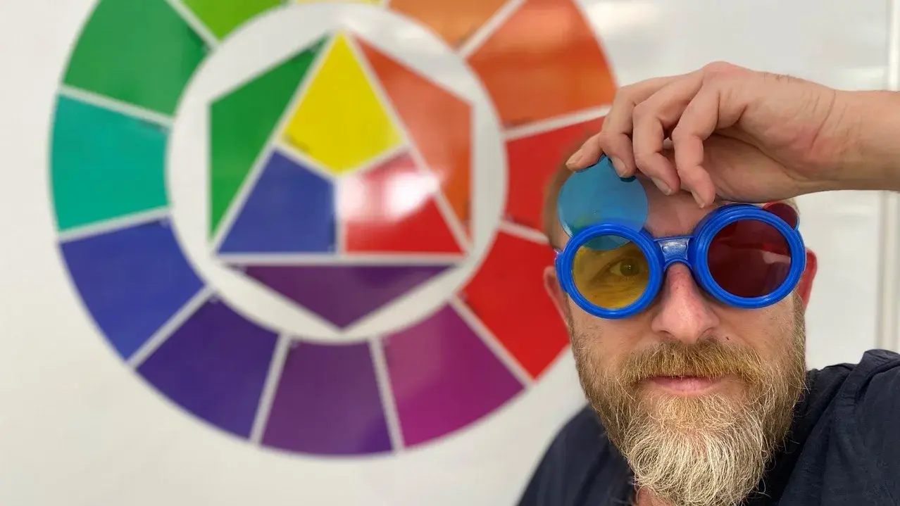 Farblabor kunst.galerie.fürth Mann mit bunter Brille vor einem Farbkreis mit Primär-, Sekundär- und Tertiärfarben